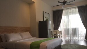 Een hotelkamer met een bed, een bureau, een stoel, een plafondventilator en een groot raam met gordijnen.