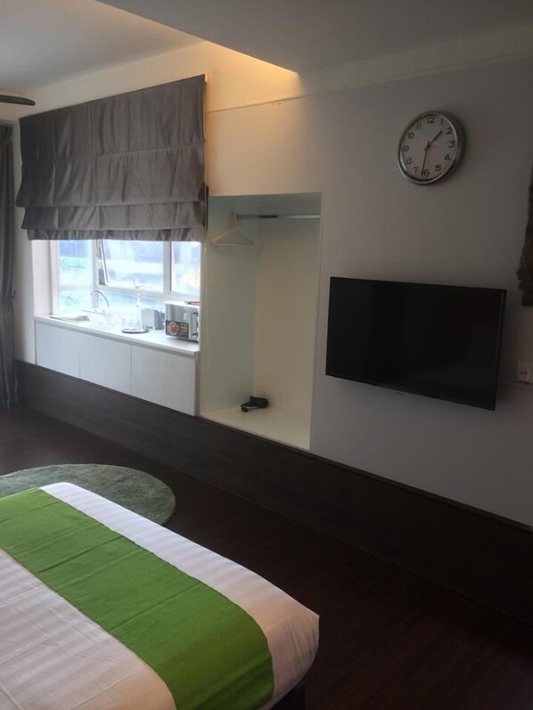 Un dormitorio con cama, ventana con vistas, televisor montado en la pared y un reloj.