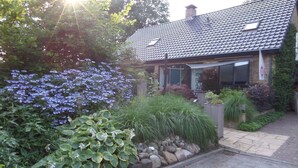 A house with a tiled roof, a stone pathway, and a variety of plants and flowers in the garden. - B&B Op de Parkkamp (Havelte)