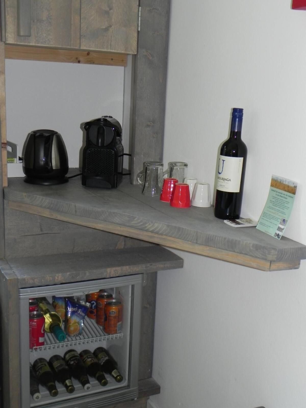 A kitchenette with a coffee maker, a wine bottle, and a refrigerator containing beverages.