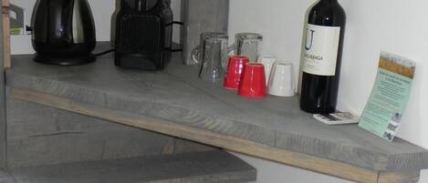 A kitchenette with a coffee maker, a wine bottle, and a refrigerator containing beverages.
