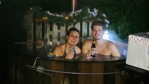 Two people in a hot tub with a wooden exterior and a chimney. - B&B Op de Parkkamp (Havelte)