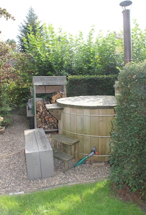 A wooden hot tub with a bench, surrounded by a gravel area and greenery. - B&B Op de Parkkamp (Havelte)