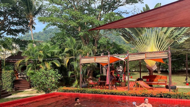 A pool area with a red-tiled border, surrounded by lush greenery and a shaded seating area with a hammock and a bicycle. - Red Moon Hideaway (Ko Chang)