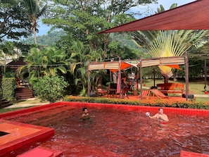 A pool area with a red-tiled border, surrounded by lush greenery and a shaded seating area with a hammock and a bicycle. - Red Moon Hideaway (Ko Chang)