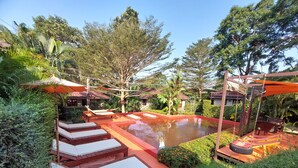 A pool area with lounge chairs and a swing chair, surrounded by lush greenery and trees. - Red Moon Hideaway (Ko Chang)