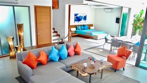 A modern living room with a grey sectional sofa, colorful cushions, a wooden coffee table, and a view of the dining area. - Ka Villa Rawai : Peaceful 4 Bedrooms (Rawai)
