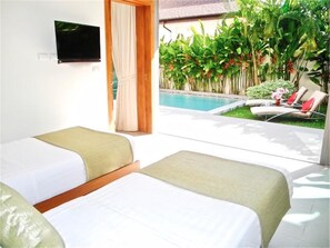 Une chambre d’hôtel avec deux lits, une télévision, une piscine et un jardin agrémenté de plantes et d’une chaise.
