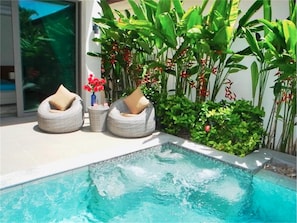 Une piscine avec deux chaises longues en osier et une petite table agrémentée de fleurs rouges.