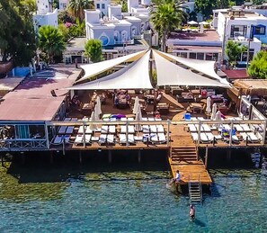 A waterfront hotel with a covered dining area, lounge chairs, and a dock.