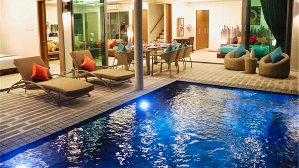 Un área de piscina interior moderna con sillones de descanso, una mesa de comedor y una escalera que conduce a un nivel superior.