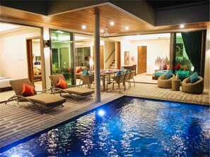 Un área de piscina interior moderna con sillones de descanso, una mesa de comedor y una escalera que conduce a un nivel superior.