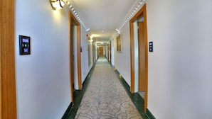 A hotel hallway with a patterned carpet, wooden doors, and illuminated wall sconces. - Marathon Hotel (Elazig)
