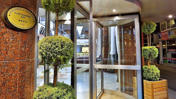 A hotel entrance with a marble wall, a plaque, and a glass door leading to the interior. - Marathon Hotel (Elazig)