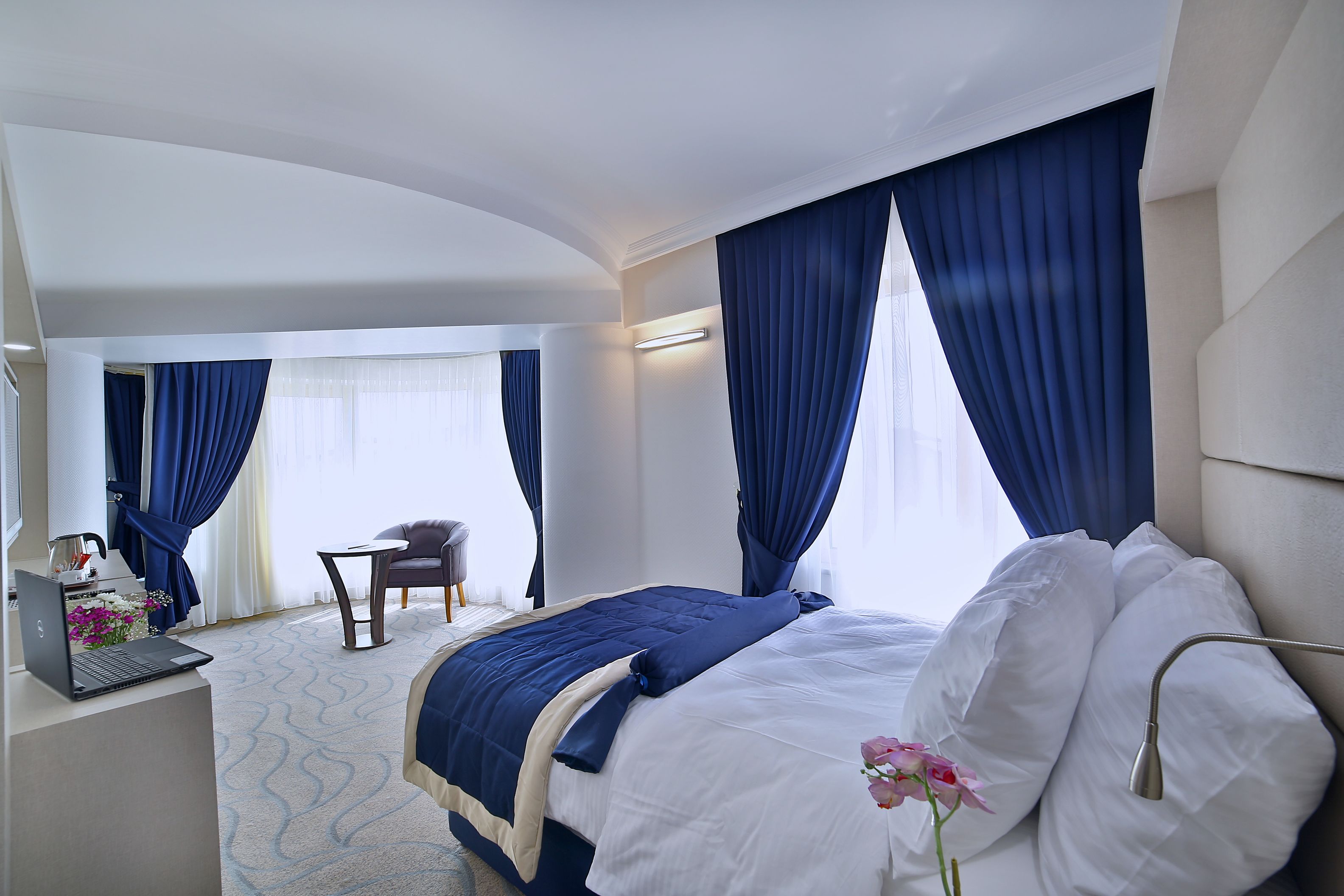 Quarto de hotel com uma cama, uma mesa de escritório com um laptop, uma cadeira e uma pequena mesa.