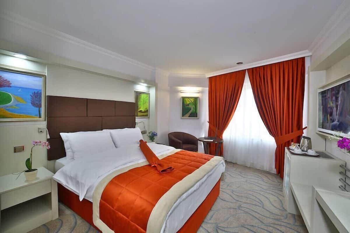 A hotel room with a large bed, a desk, a chair, a TV, and a window with curtains.