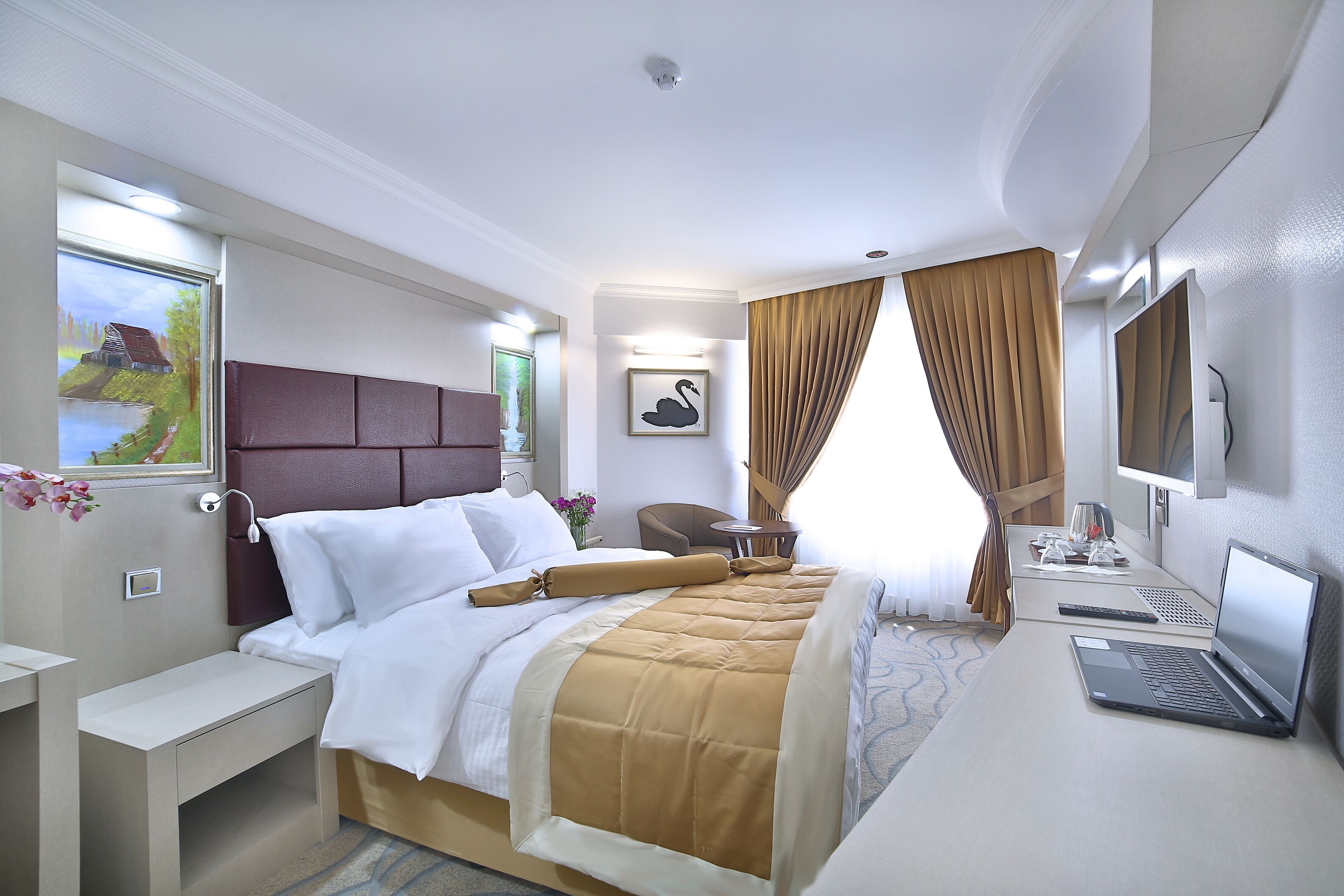 Habitación de hotel con cama, escritorio, computadora portátil, televisión y un cuadro en la pared.