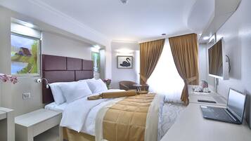 Habitación de hotel con cama, escritorio, computadora portátil, televisión y un cuadro en la pared.