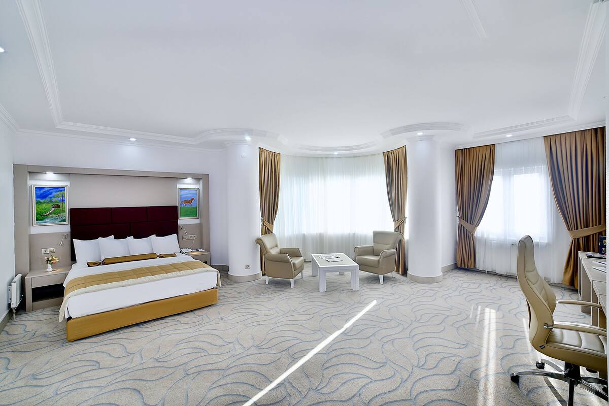 A hotel room with a large bed, two armchairs, a small table, and a desk.