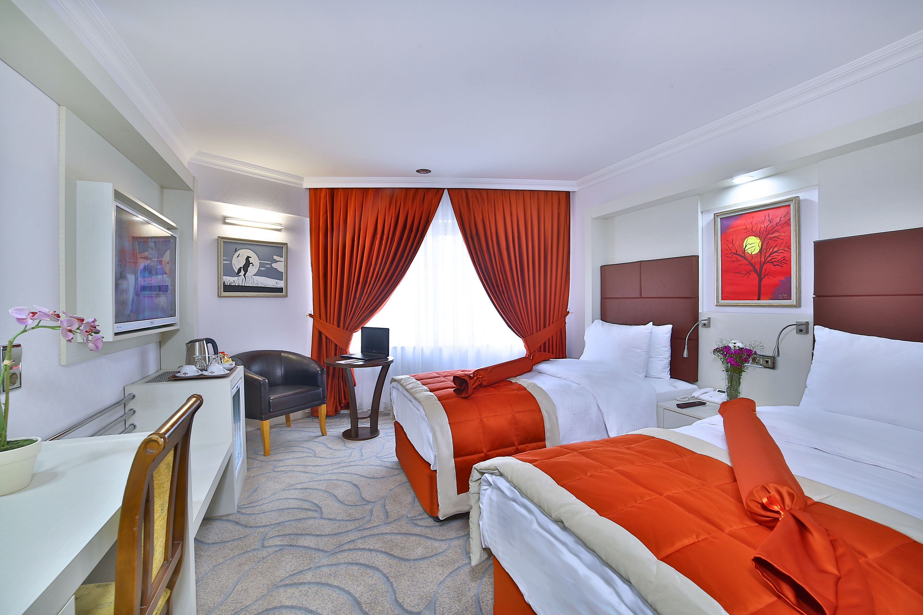 A hotel room with two beds, a desk, a chair, a TV, and a painting on the wall.