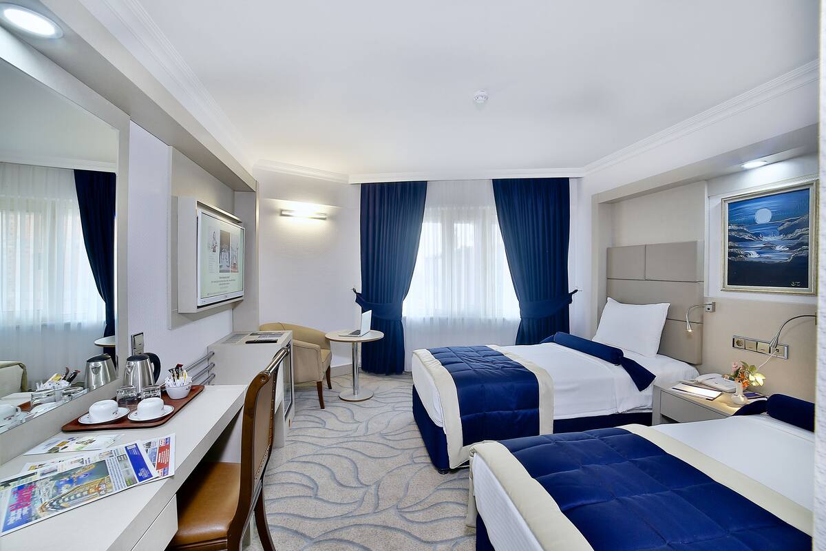 A hotel room with two beds, a desk with a chair, a small table, and a large mirror.