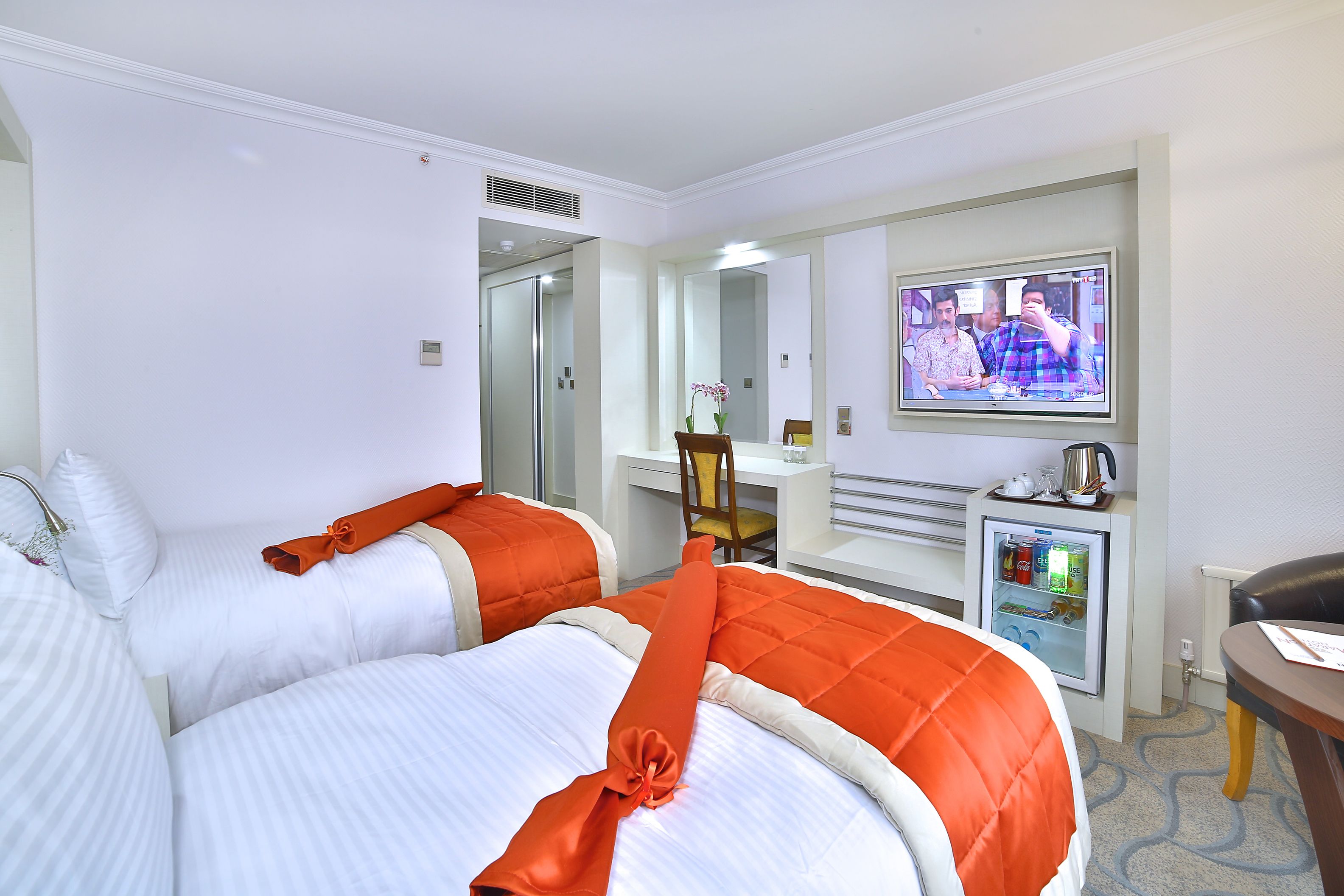 A hotel room with two beds, a desk, a television, and a minibar.