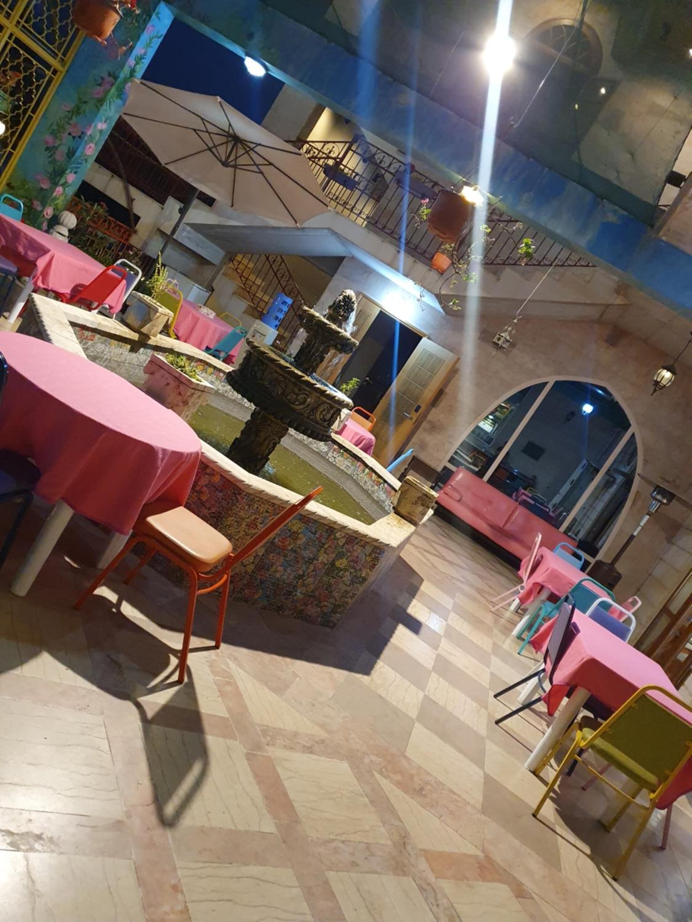 A restaurant with tiled flooring, tables with pink tablecloths, and a decorative fountain.