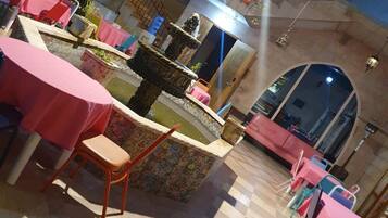 A restaurant with tiled flooring, tables with pink tablecloths, and a decorative fountain.