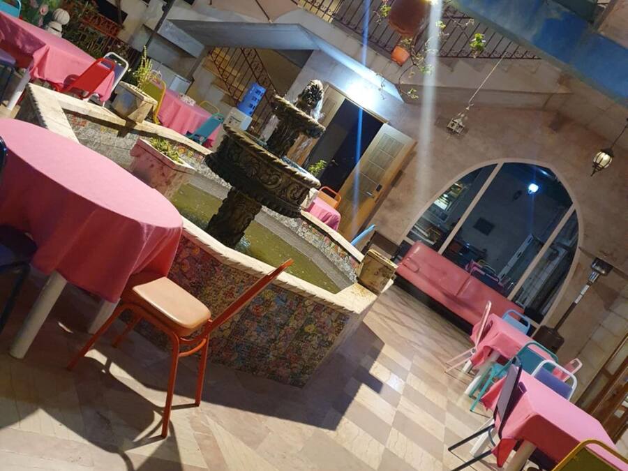 A restaurant with tiled flooring, tables with pink tablecloths, and a decorative fountain.