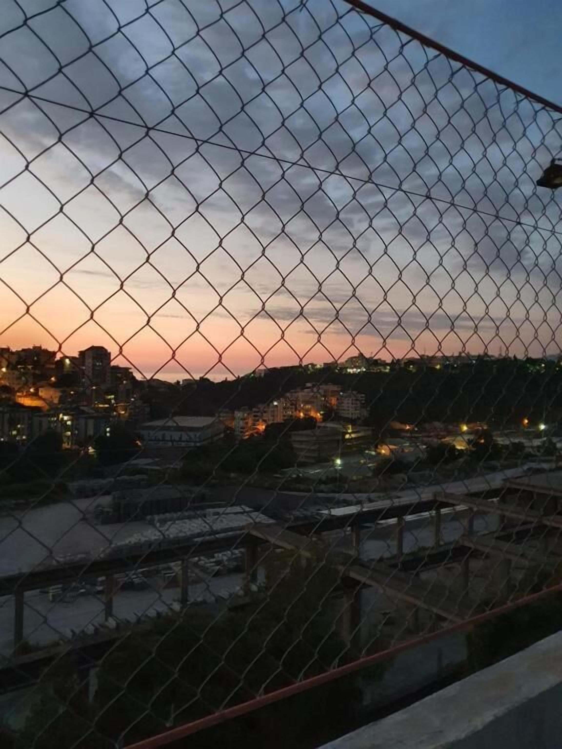 Metallinen linkkiaita, jonka takaa avautuu näkymä kaupungin siluettiin auringonlaskun aikaan.