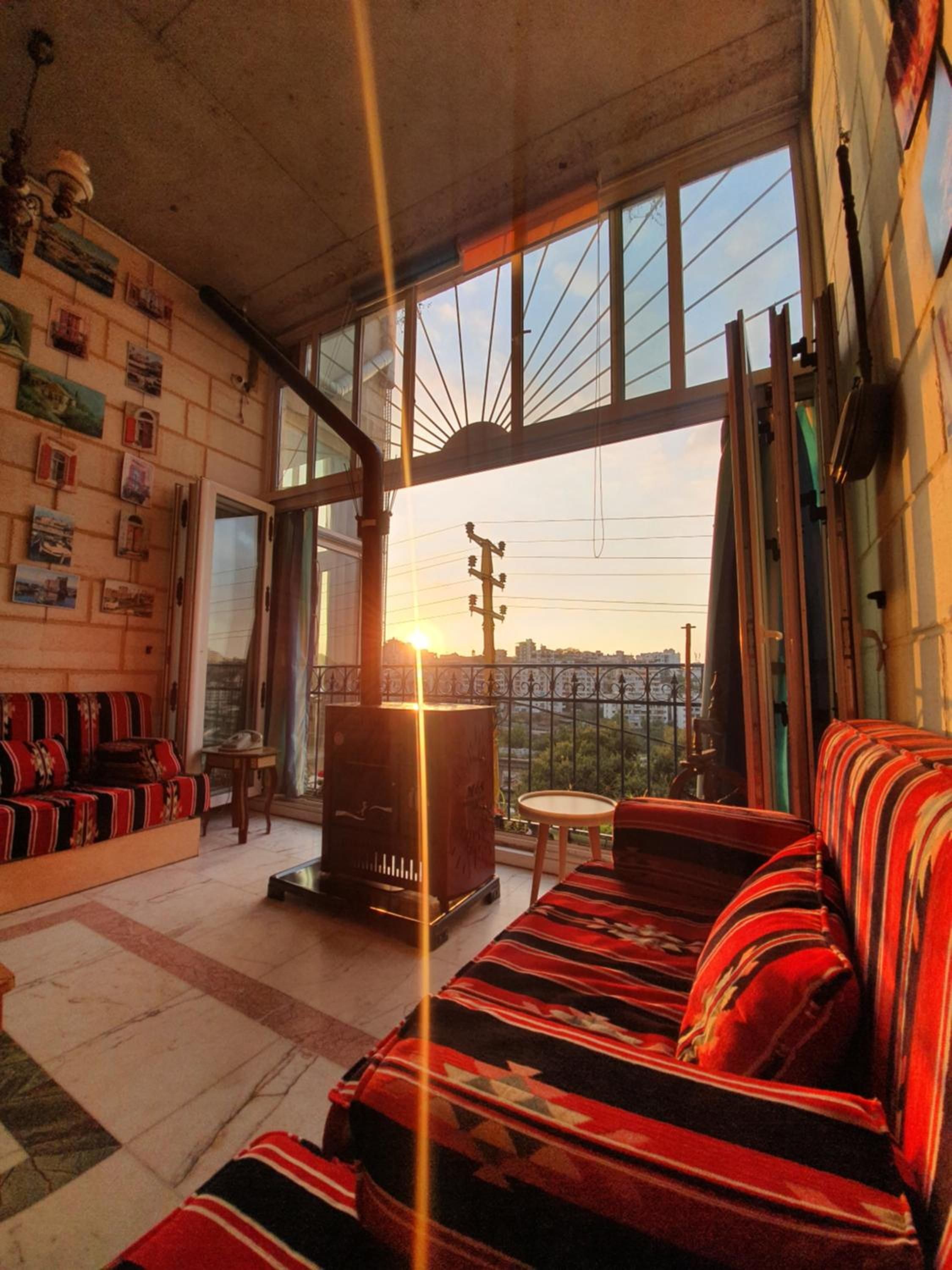 A cozy living room with a sofa, a small table, and a fireplace. There are large windows offering a view of the cityscape.