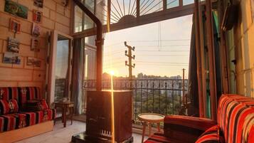 A cozy living room with a sofa, a small table, and a fireplace. There are large windows offering a view of the cityscape.