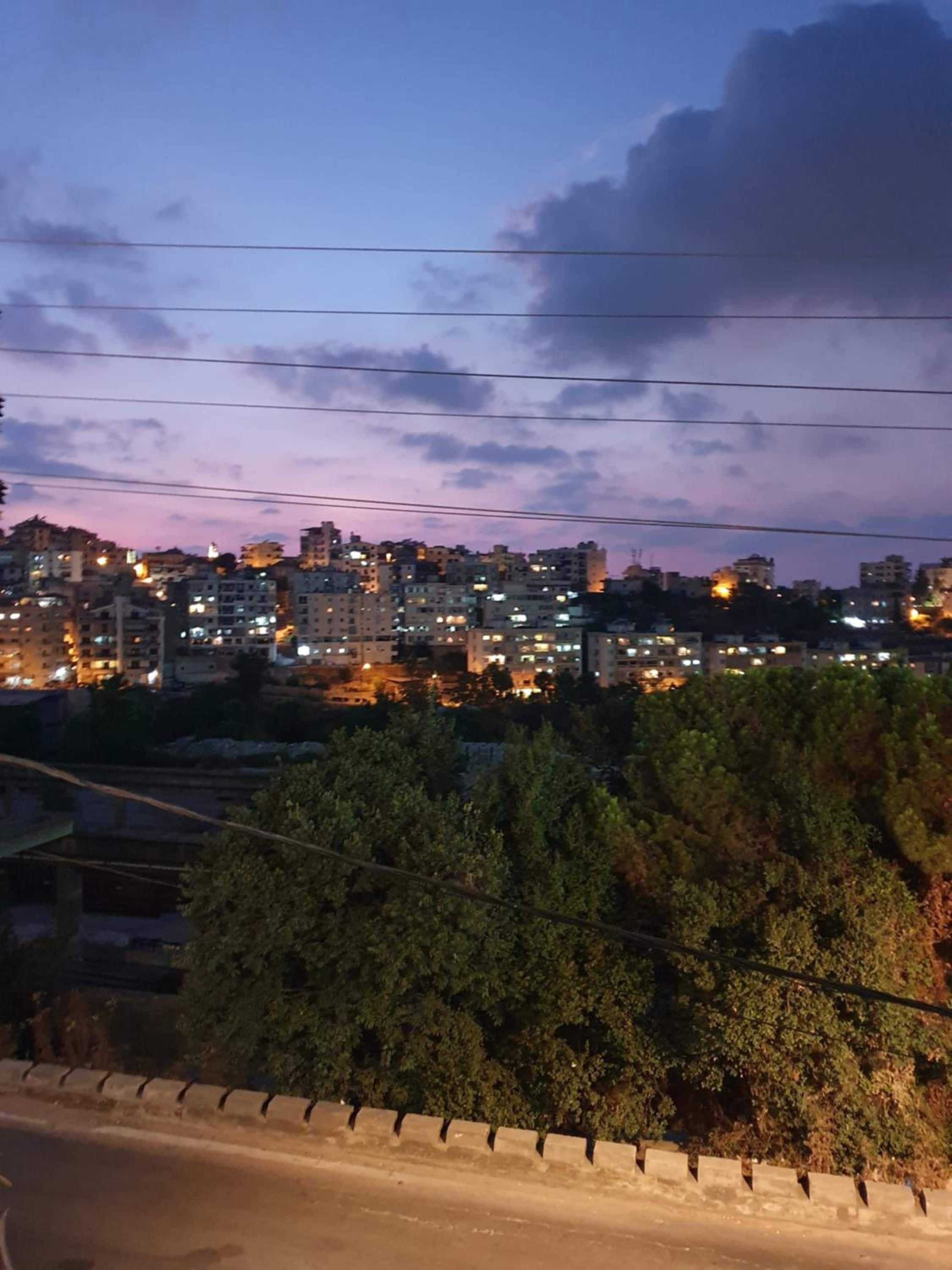 Une vue sur une ville au crépuscule, avec des bâtiments illuminés se détachant sur un ciel teinté de couleurs crépusculaires.