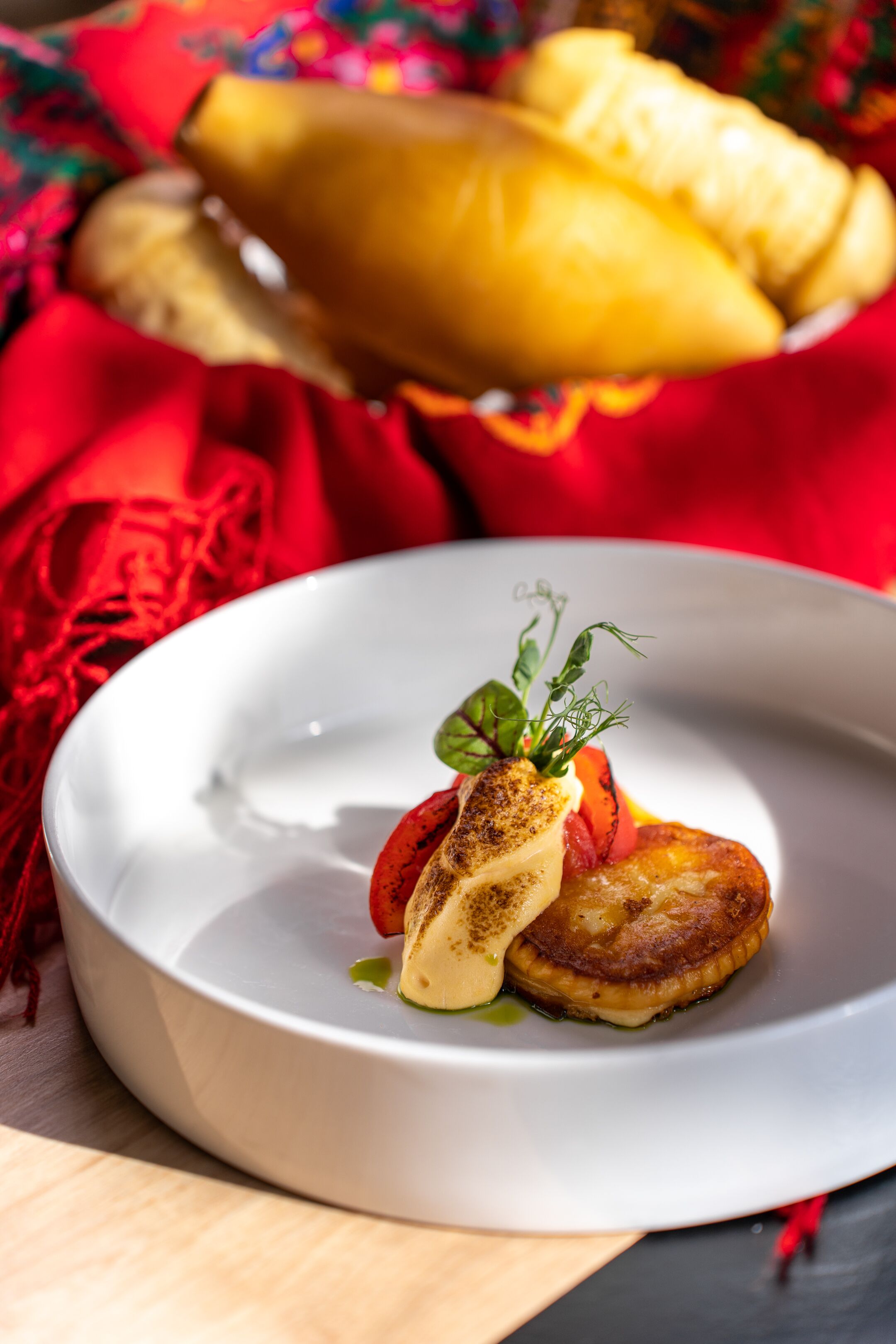 A white plate with a grilled patty, a slice of cheese, and a garnish on a wooden table with a red cloth.
