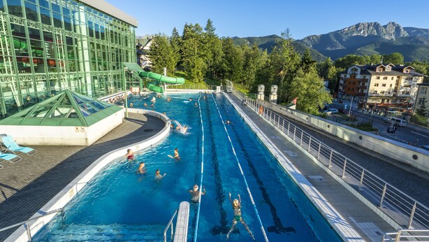 Une piscine avec des couloirs bien délimités, un toboggan aquatique et une vue sur les montagnes en arrière-plan.