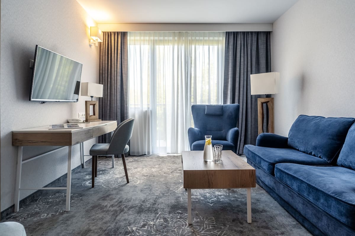 A modern hotel room with a flat-screen TV, a desk with a chair, a blue sofa, and a coffee table.