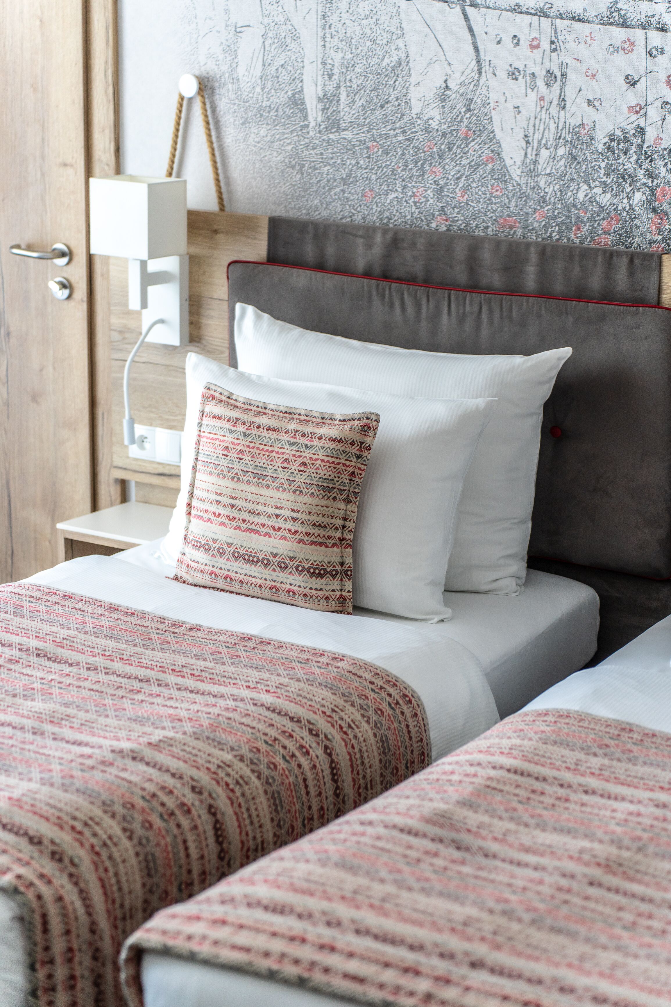 A bedroom with a bed, two pillows, a nightstand, and a wall with a floral pattern.