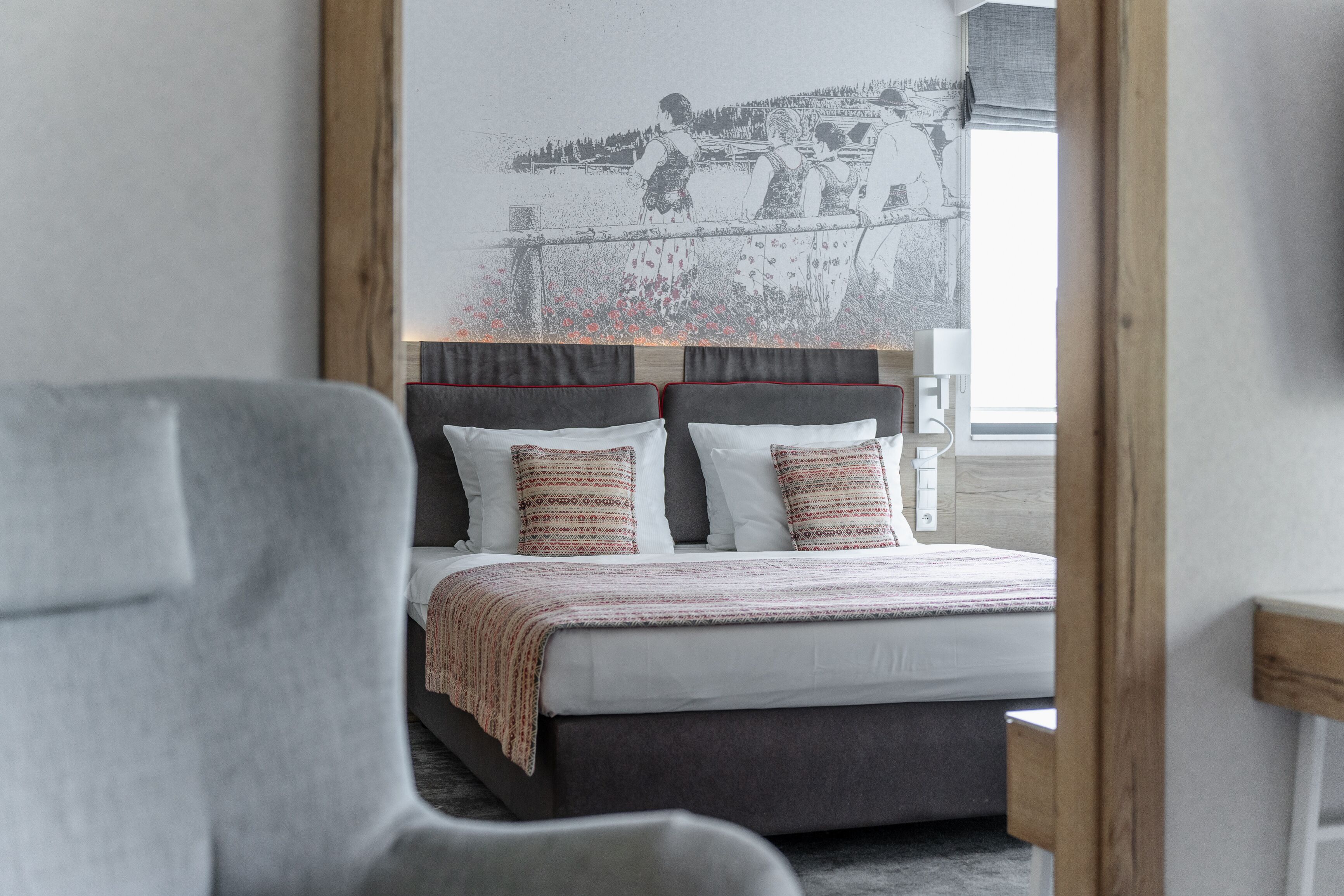 A modern bedroom with a large bed, a headboard with a mirror, and a view of a lake through the window.