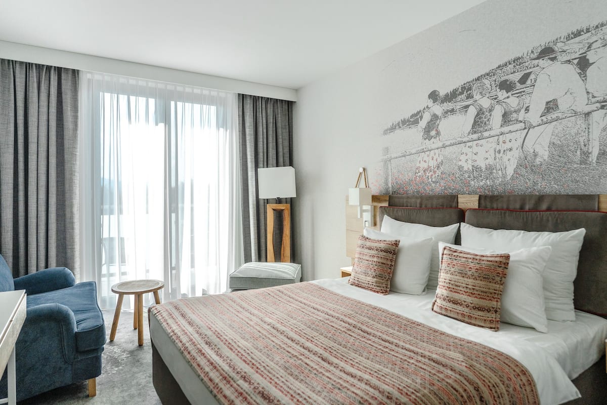 A hotel room with a bed, a chair, a small table, and a lamp.