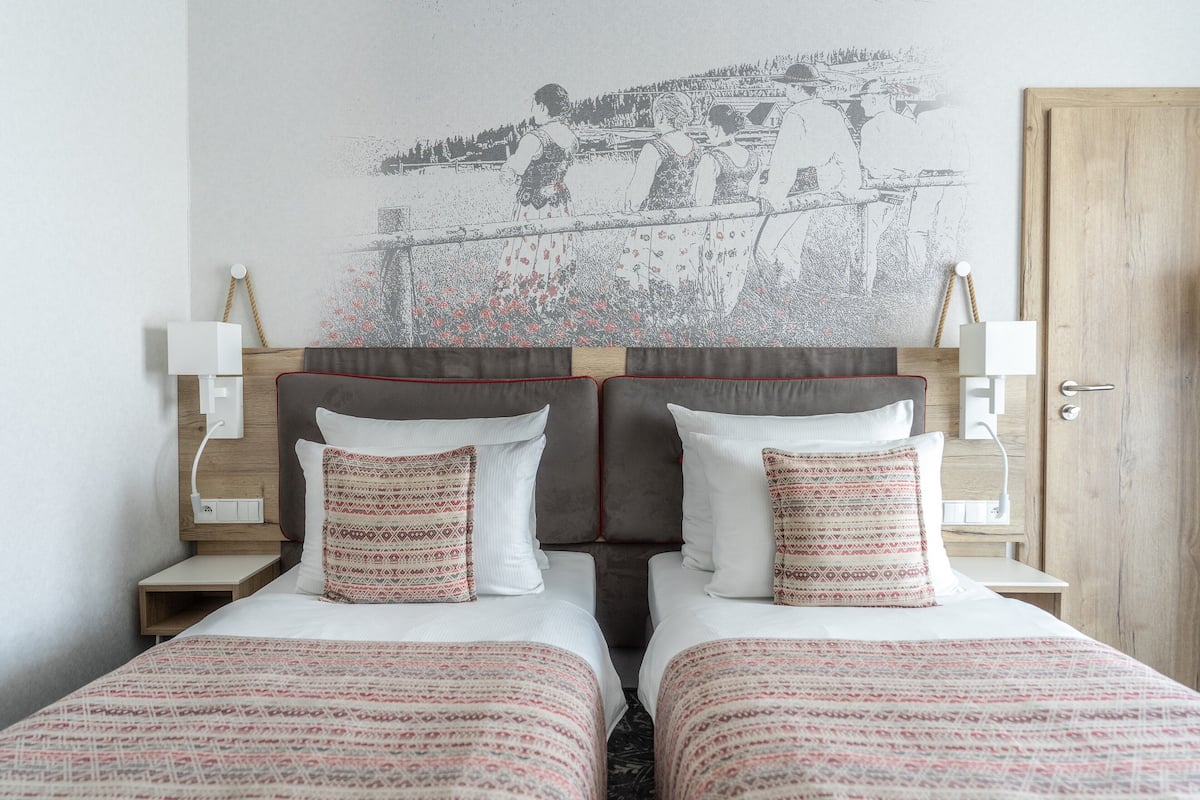 A hotel room with two beds, a headboard with a mural, bedside tables with lamps, and a wooden door.
