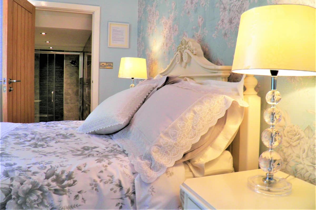 A bedroom with a bed, two bedside lamps, a door, and a shower area.