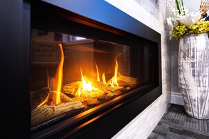 Una chimenea moderna con frente de vidrio, un marco de mármol y un jarrón con flores a la derecha.