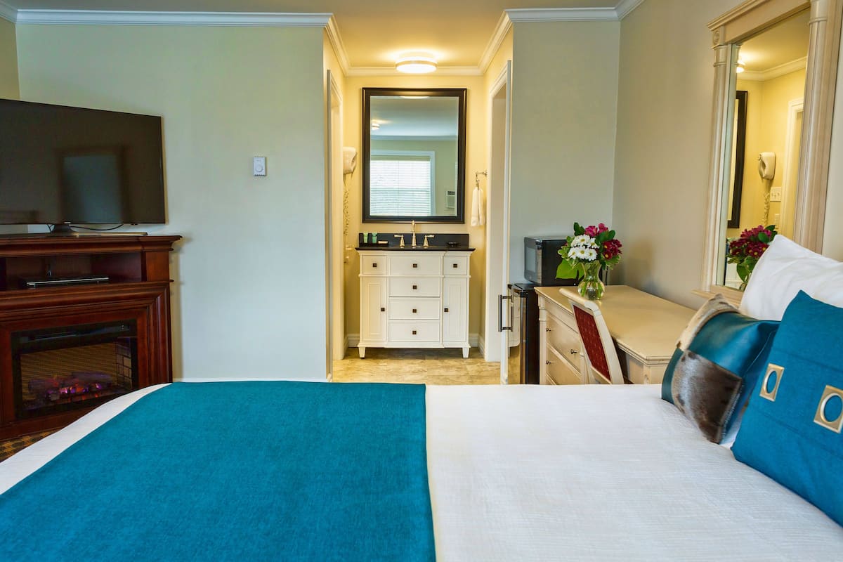 A hotel room with a bed, a TV, a dresser, a mirror, and a bathroom visible through an open door.