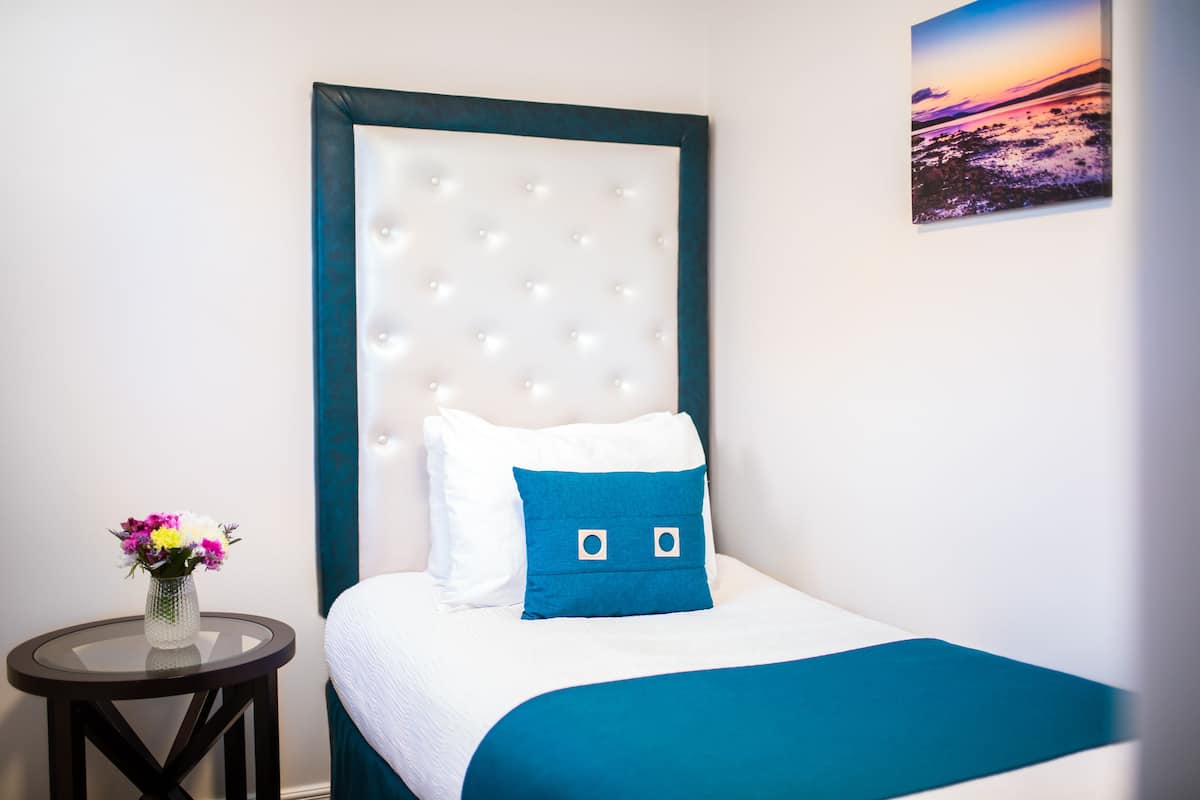 A neatly arranged hotel room with a bed, a round table with a vase of flowers, and a framed picture on the wall.
