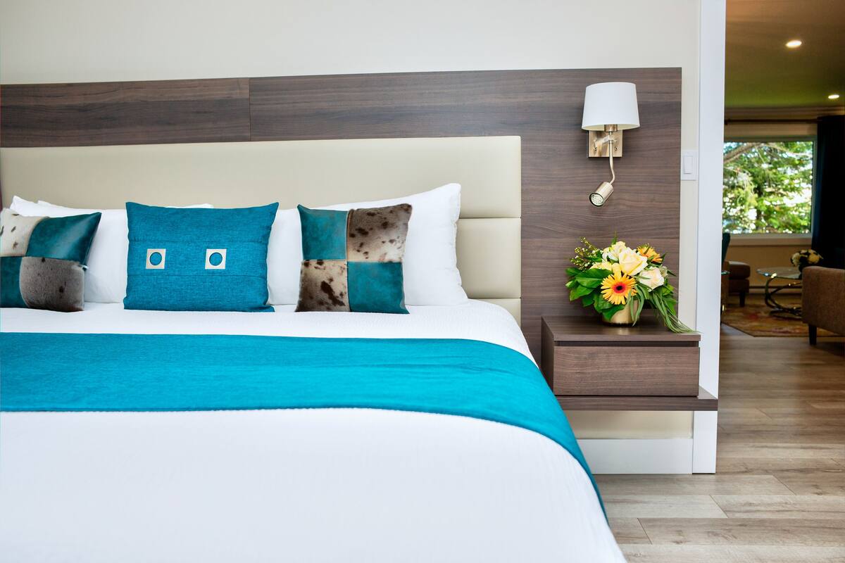 A modern hotel room with a large bed, a nightstand with a vase of flowers, and a view of the outdoors.
