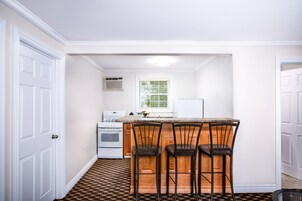 Una cocina con paredes blancas, encimera de madera y tres taburetes de bar.