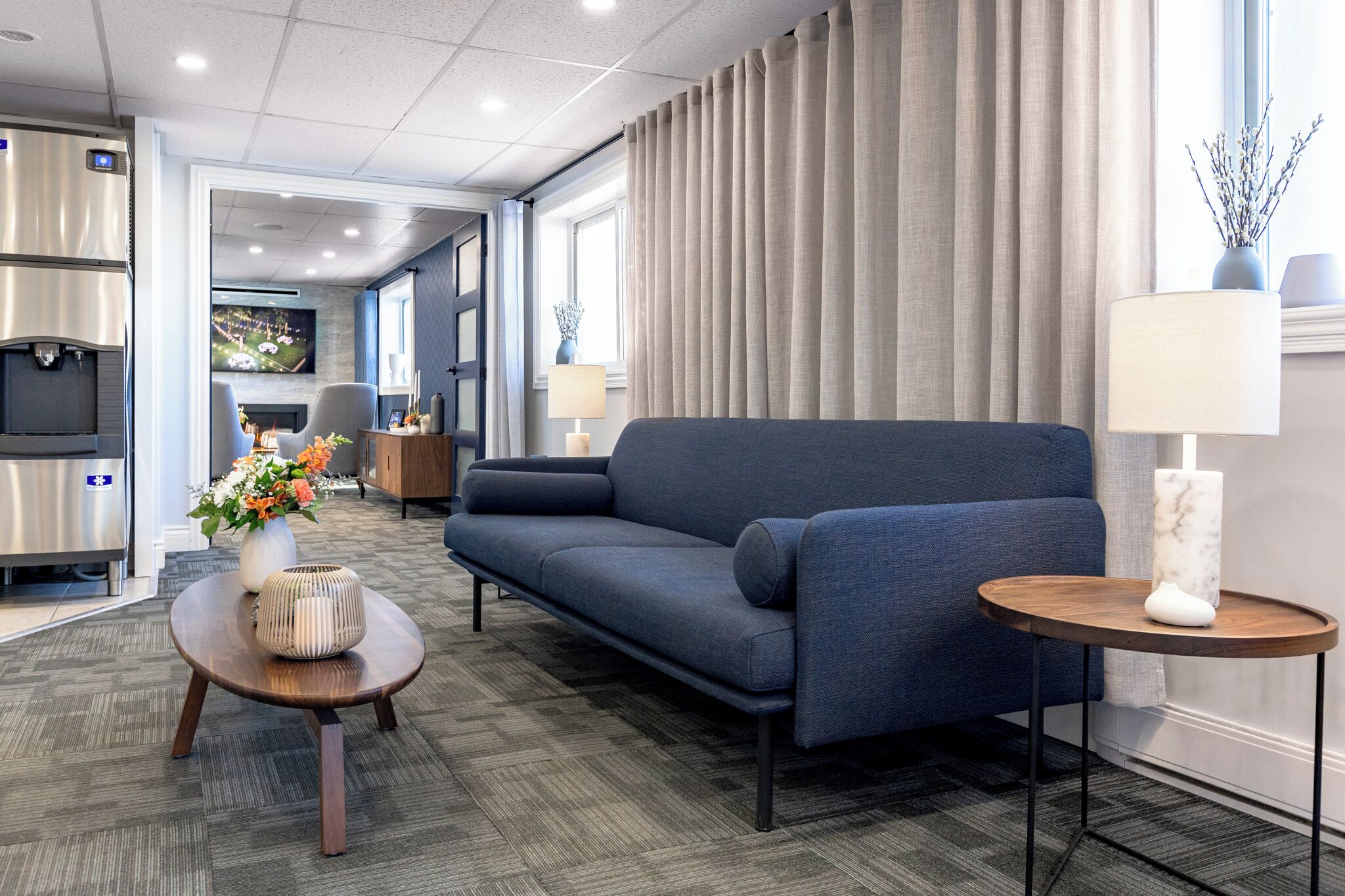 A modern hotel room with a sofa, a small round table, a TV, and a kitchen area.