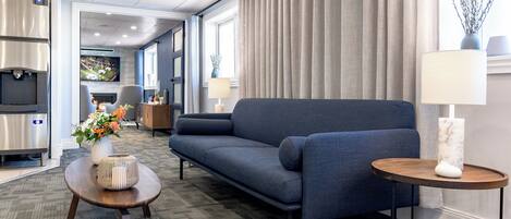 A modern hotel room with a sofa, a small round table, a TV, and a kitchen area.