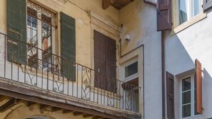 A courtyard with a stone floor, a balcony with wrought iron railings, and a building with yellow and brown doors. - Suite del Doge 2 (Verona)