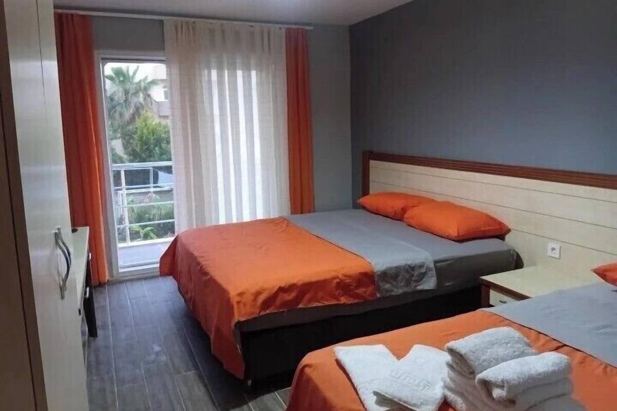 A hotel room with two beds, a balcony, and a view of greenery.